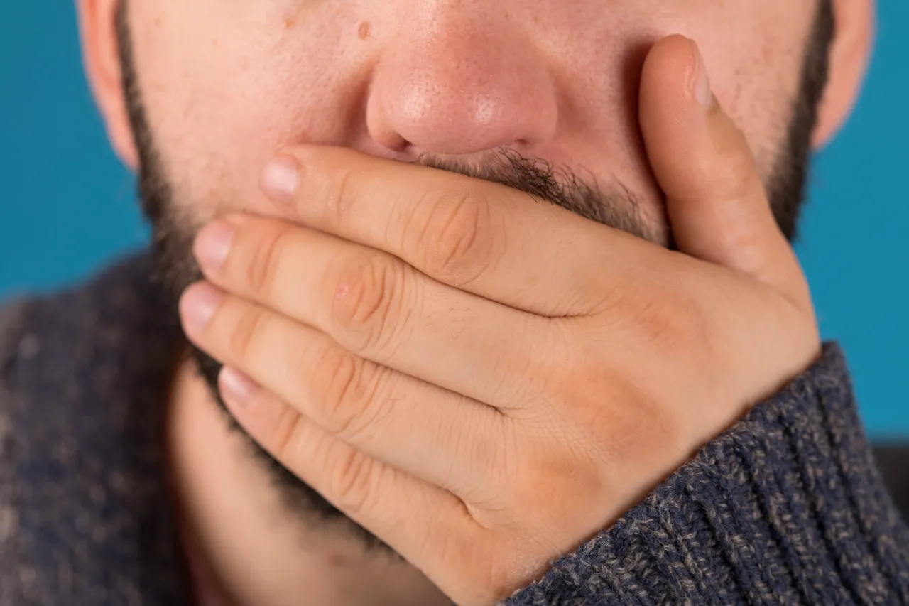 closeup of a man covering his mouth with a hand utc
