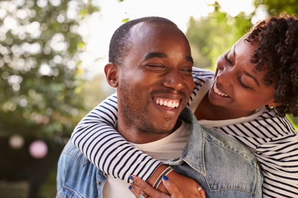 smiling young black couple piggyback in garden ey utc